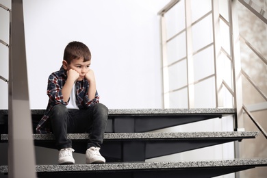 Photo of Sad little boy sitting on stairs indoors