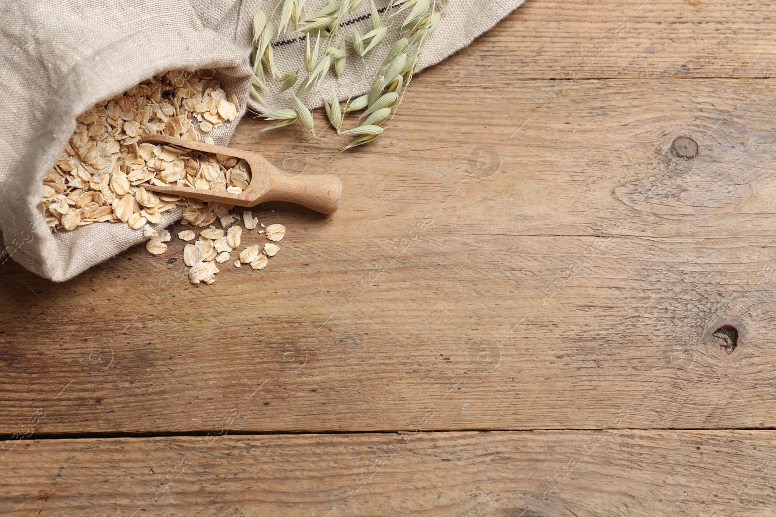 Photo of Bag with oatmeal, floret branches and scoop on wooden table, flat lay. Space for text