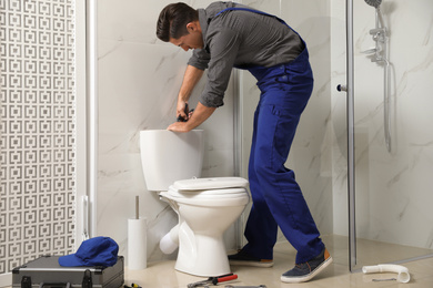 Professional plumber working with toilet bowl in bathroom