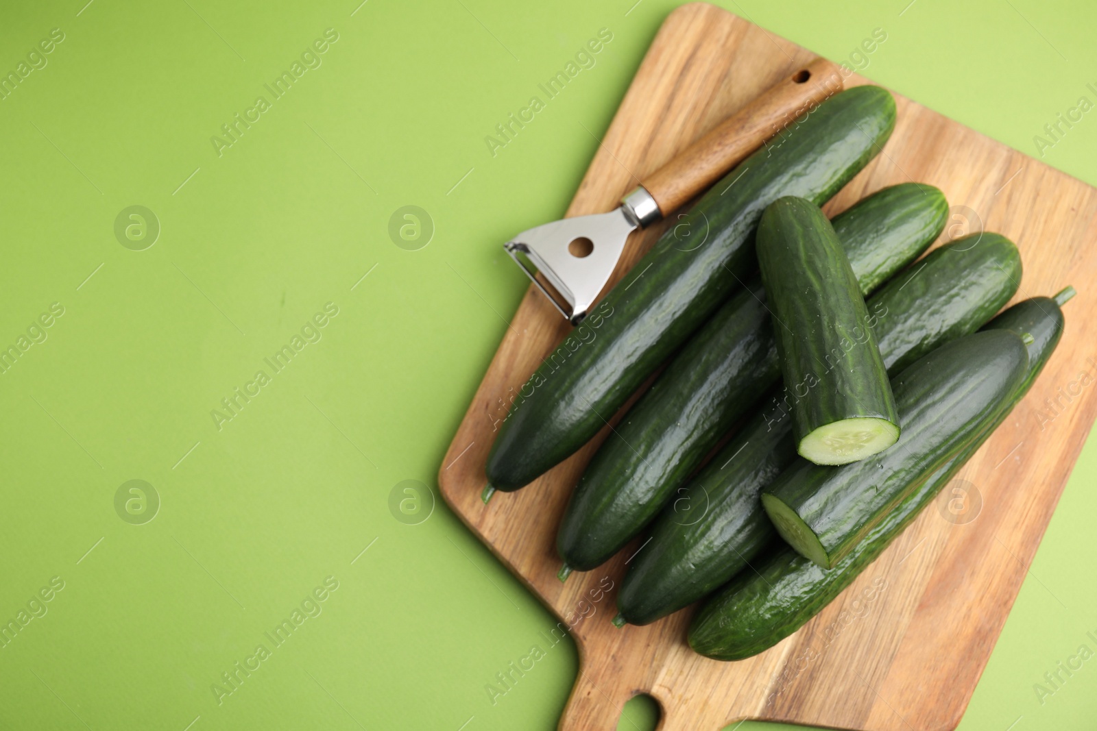 Photo of Fresh cucumbers and peeler on green background, top view. Space for text