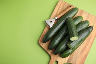 Photo of Fresh cucumbers and peeler on green background, top view. Space for text