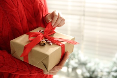 Photo of Woman holding Christmas gift box indoors, closeup. Space for text