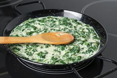 Photo of Tasty spinach dip with wooden spoon in frying pan on kitchen stove