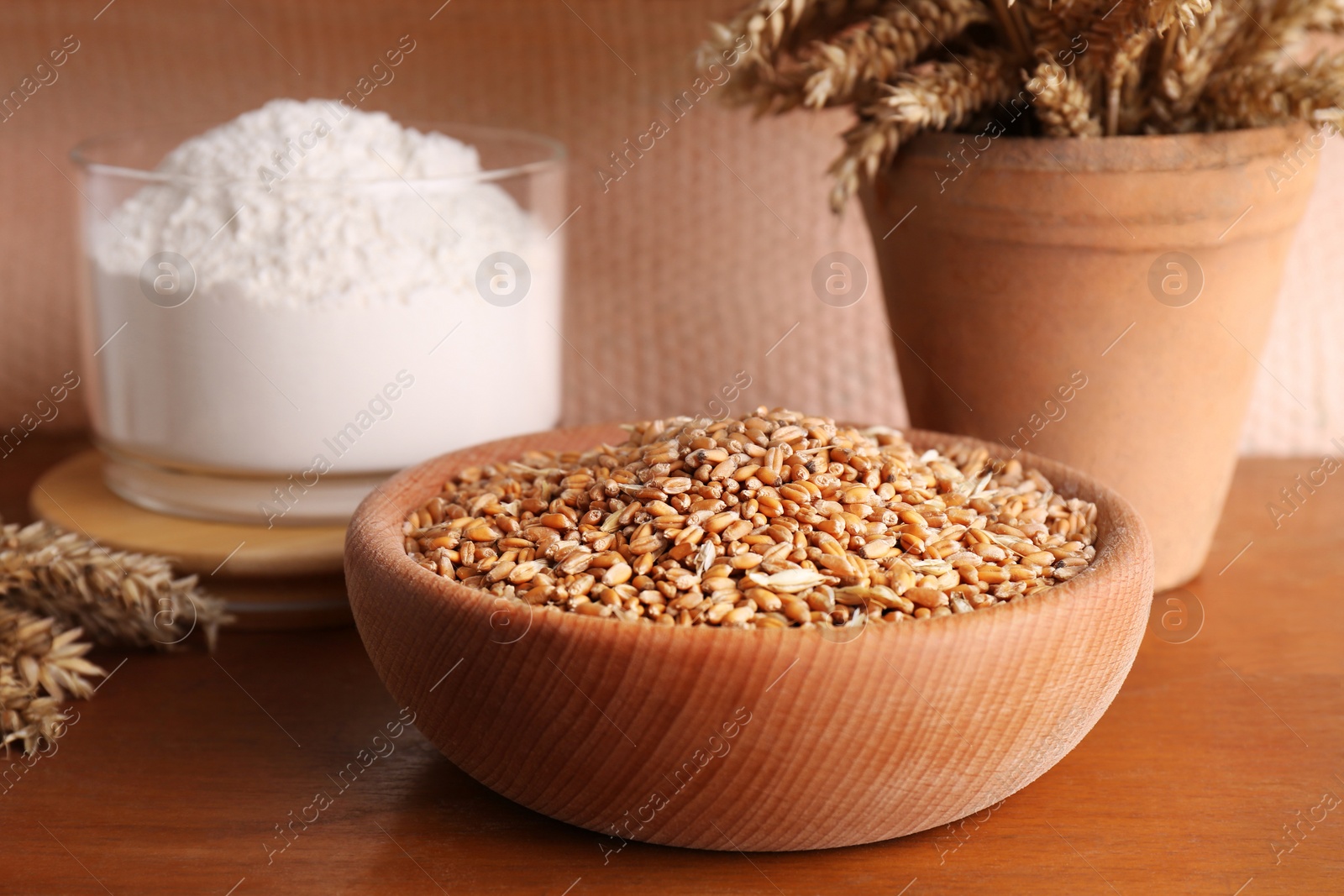 Photo of Wheat grains in bowl, spikes and flour on wooden table