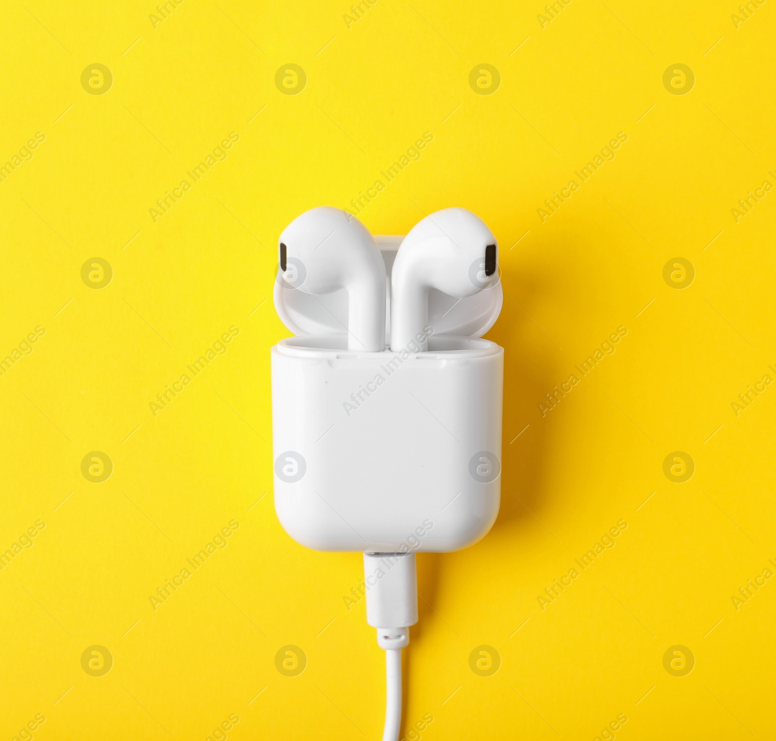 Photo of Modern wireless earphones in charging case with cable on yellow background, top view