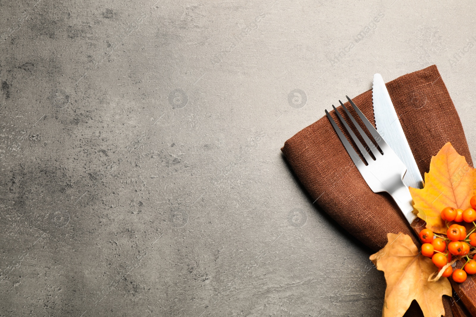 Photo of Top view of cutlery with napkin, ashberries and autumn leaves on grey table, space for text. Thanksgiving Day