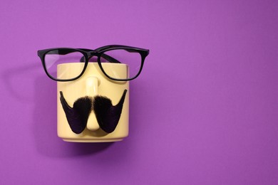 Man's face made of artificial mustache, cup and glasses on purple background, top view. Space for text