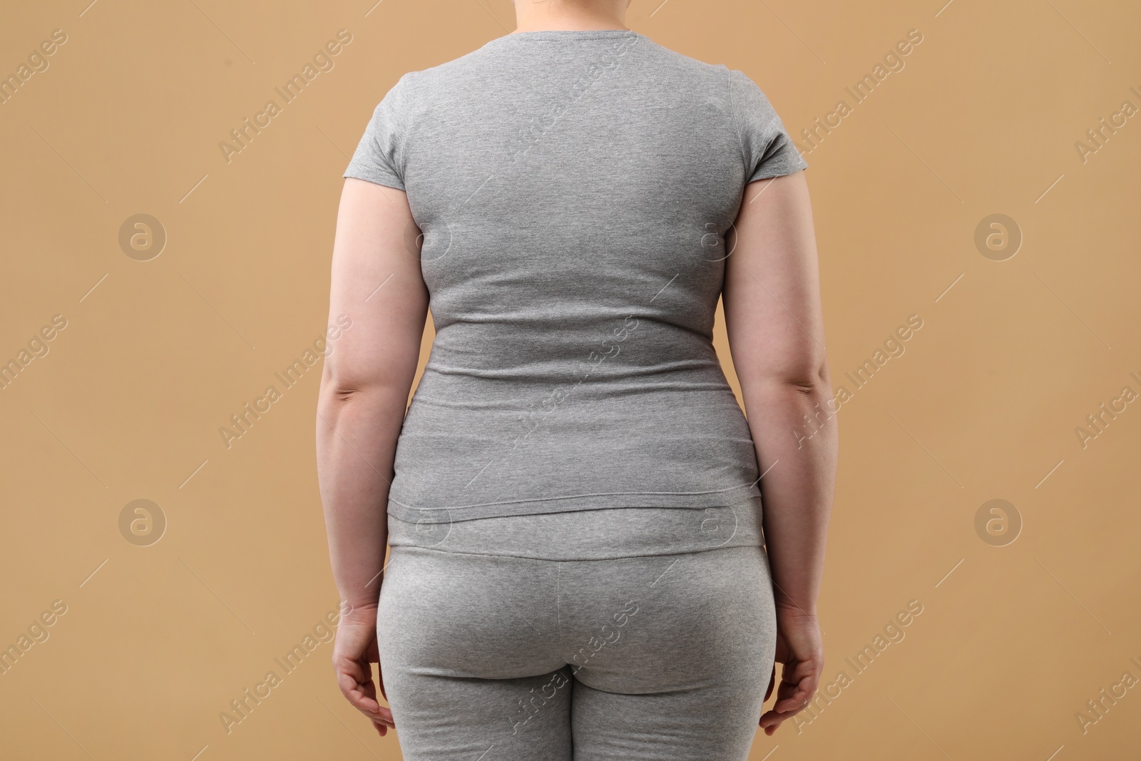 Photo of Overweight woman in grey clothes on beige background, back view