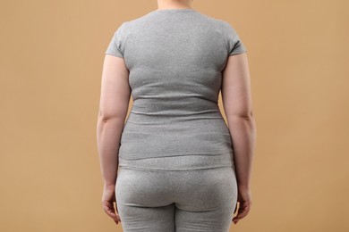 Photo of Overweight woman in grey clothes on beige background, back view