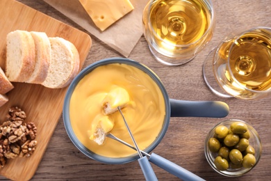 Photo of Flat lay composition with pot of cheese fondue and wine on wooden table