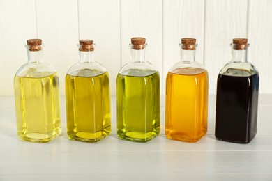 Photo of Vegetable fats. Different cooking oils in glass bottles on white wooden table