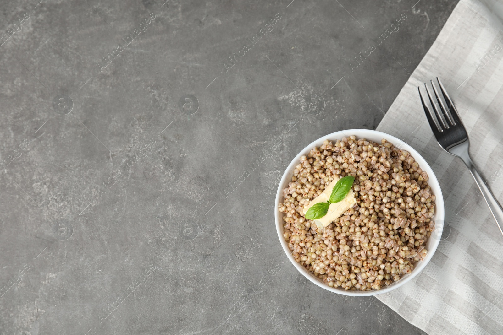 Photo of Tasty buckwheat porridge with butter on grey table, flat lay. Space for text