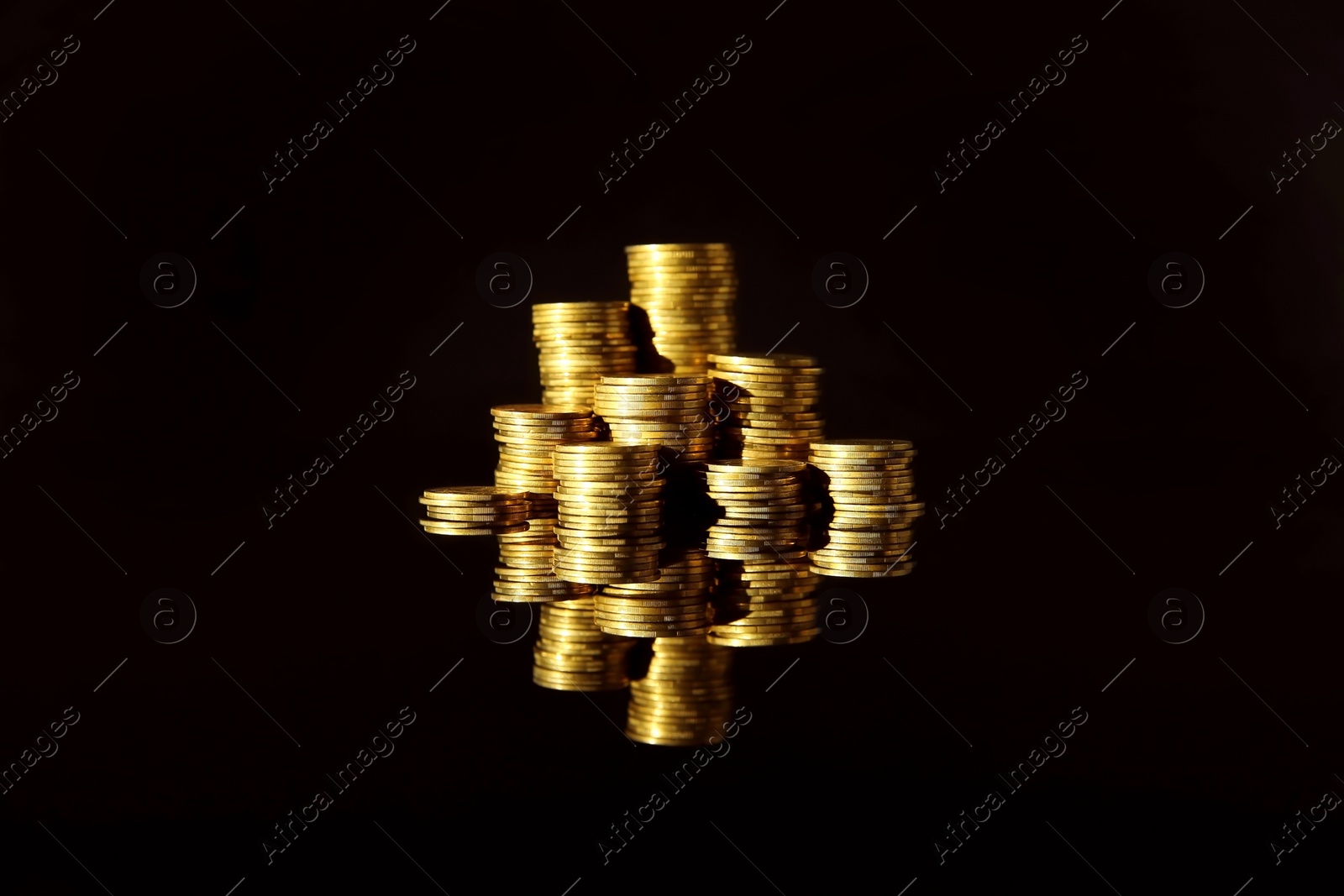 Photo of Many stacks of coins on mirror surface against black background