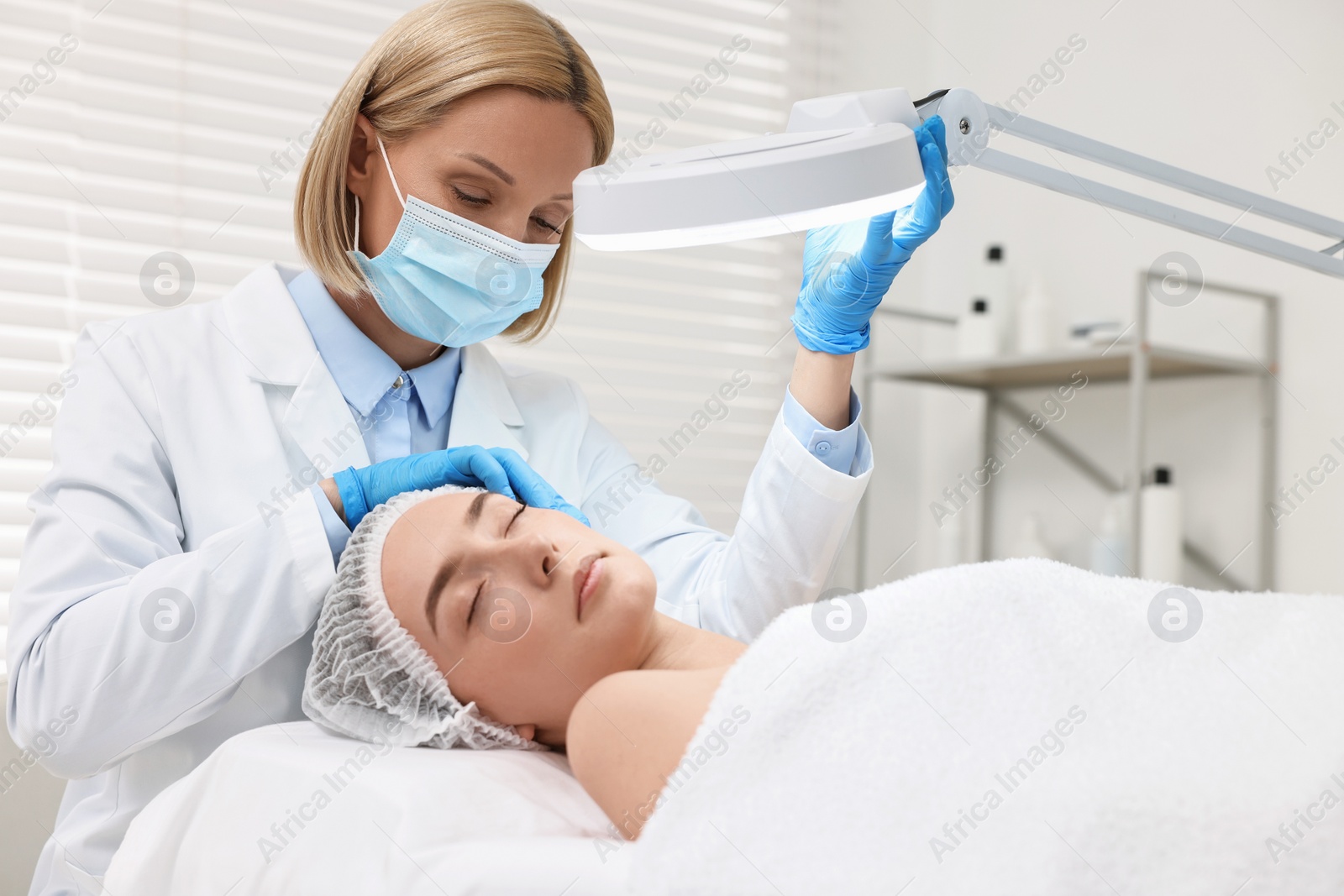 Photo of Dermatologist examining patient`s face under lamp in clinic