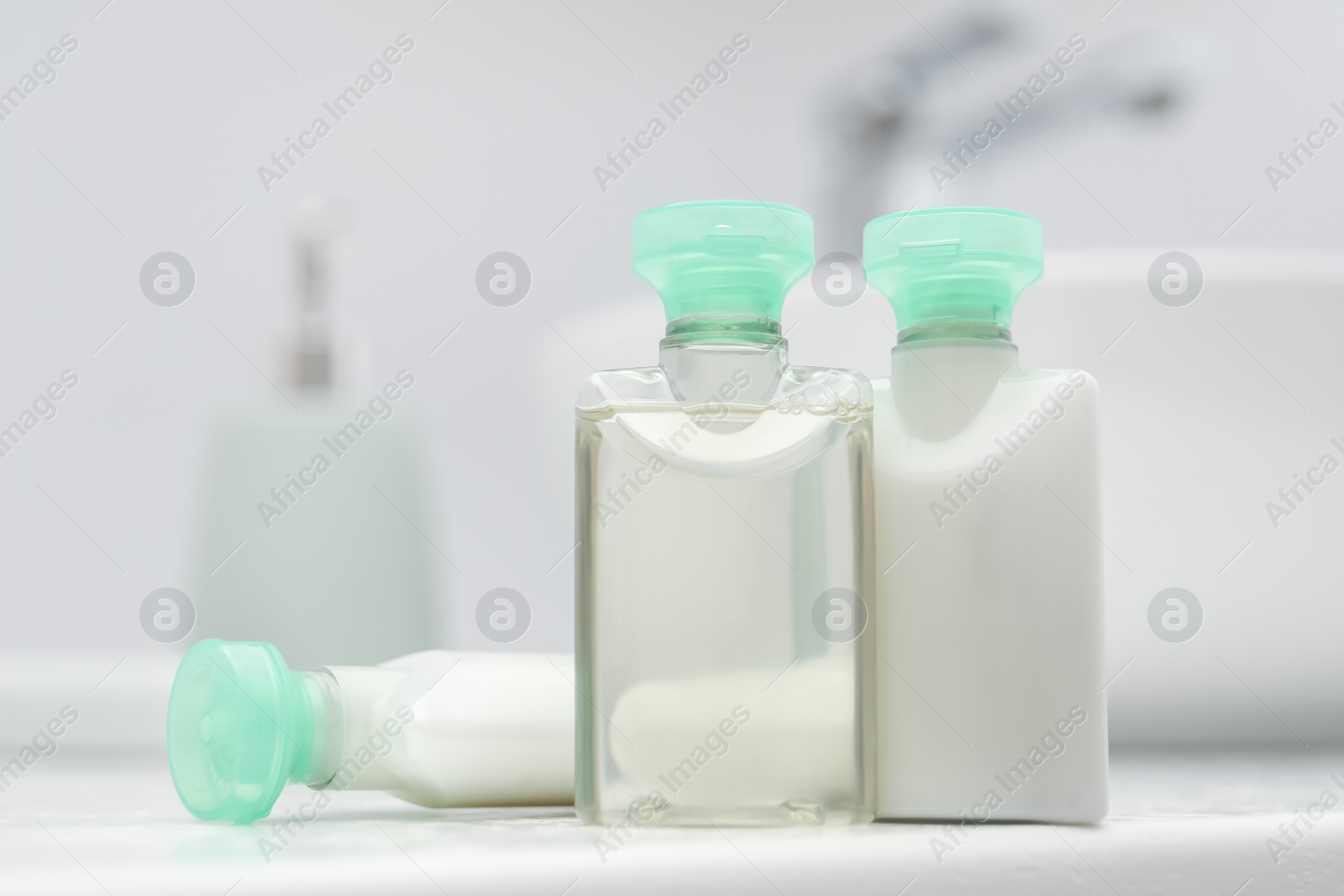 Photo of Mini bottles of cosmetic products on white countertop in bathroom, closeup