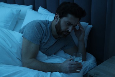 Man with glass of water suffering from headache in bed at night