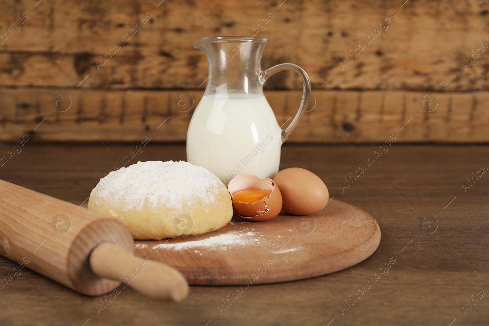 Photo of Raw eggs, dough and milk on wooden table. Baking pie