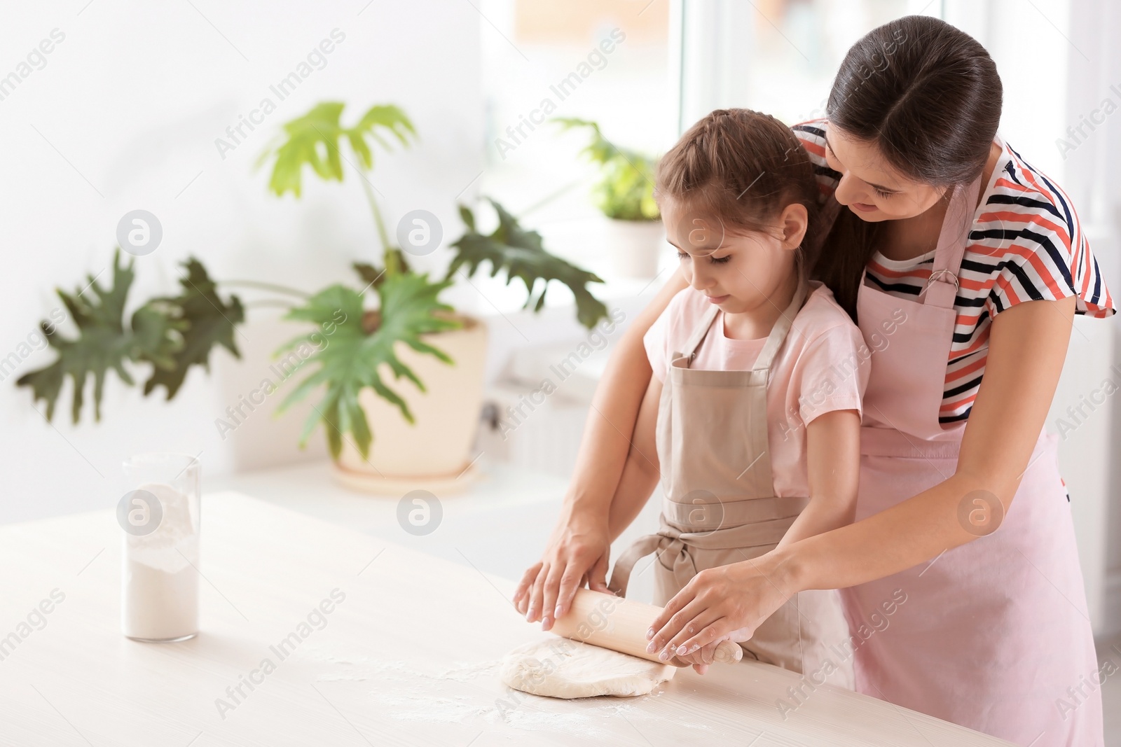 Photo of Mother and her daughter preparing dough at table in kitchen