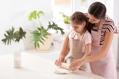 Mother and her daughter preparing dough at table in kitchen