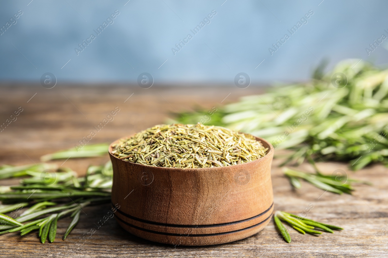 Photo of Bowl of dried rosemary and fresh leaves wooden on table