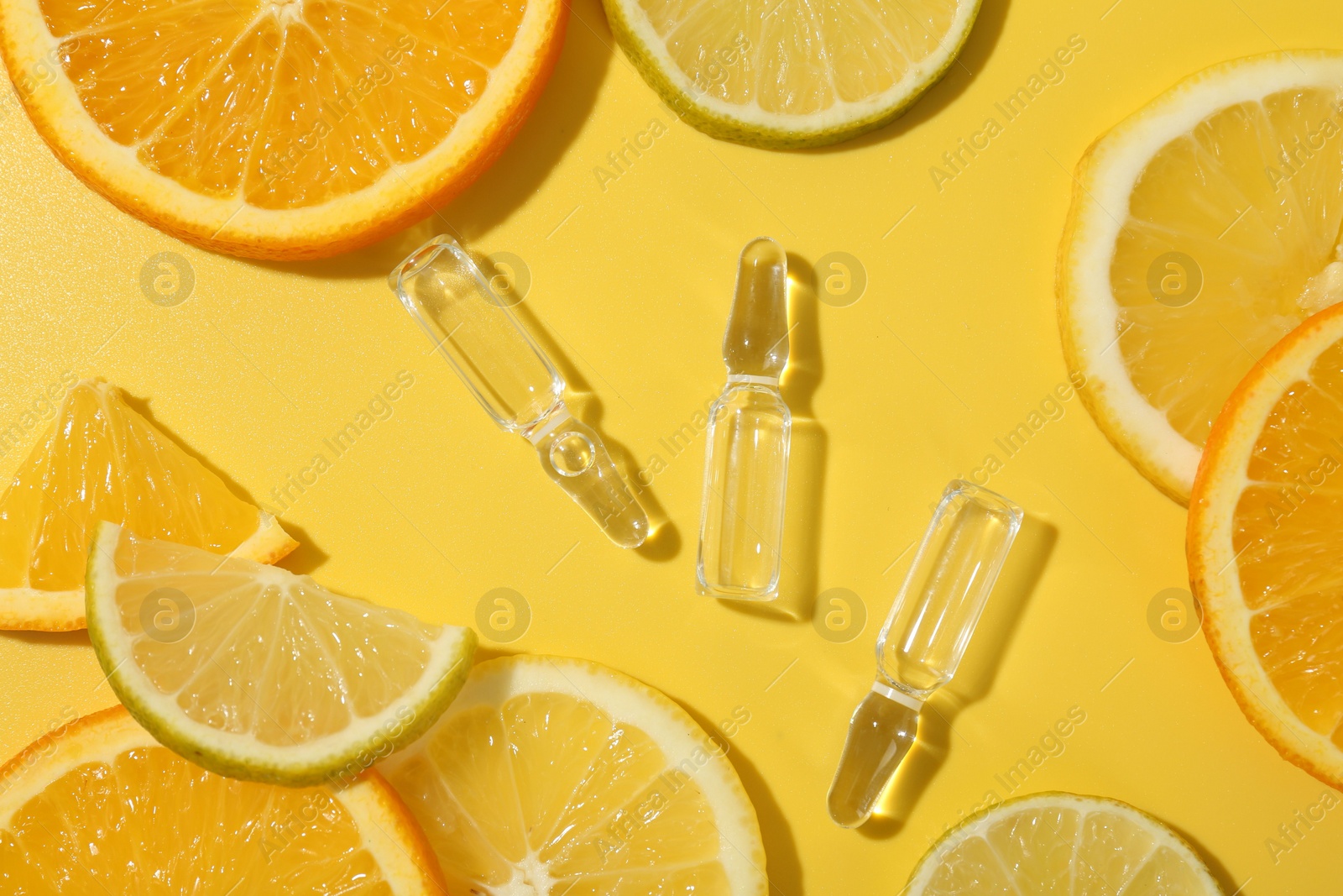 Photo of Skincare ampoules with vitamin C and citrus slices on yellow background, flat lay