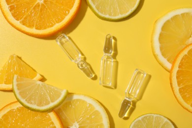 Skincare ampoules with vitamin C and citrus slices on yellow background, flat lay