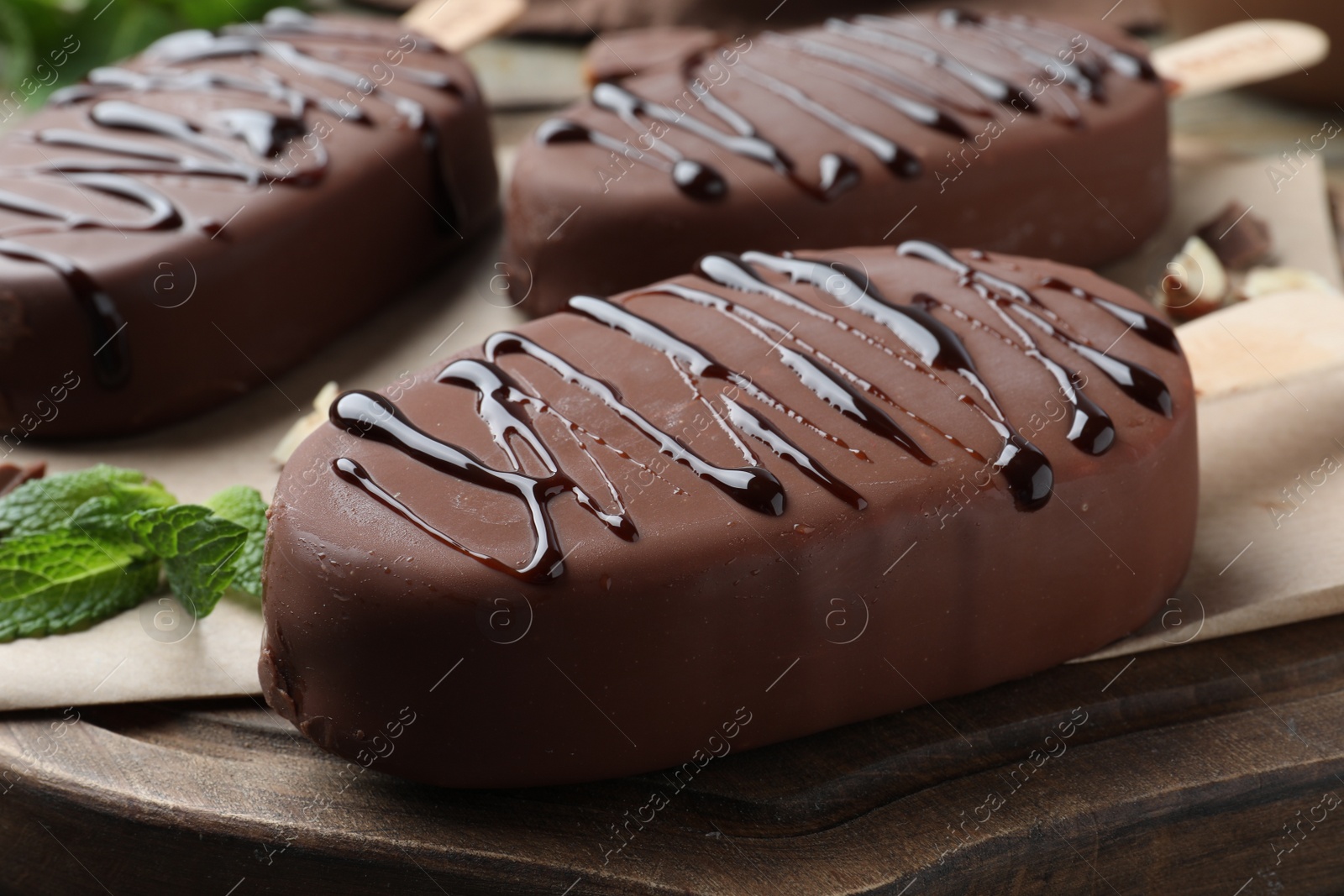 Photo of Delicious glazed ice cream bars and mint on wooden board, closeup