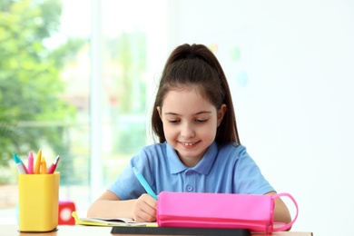 Photo of Little girl doing assignment at desk in classroom. School stationery