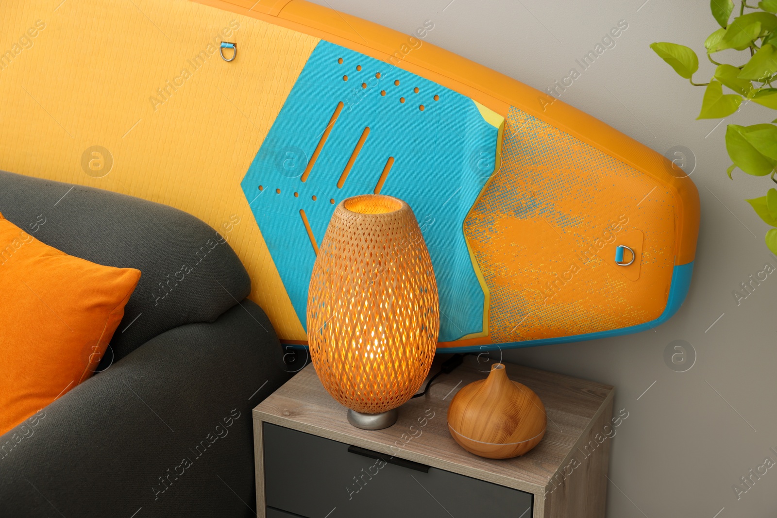 Photo of SUP board behind stylish sofa in room. Interior element