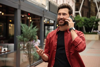 Photo of Handsome man talking on smartphone while walking outdoors, space for text
