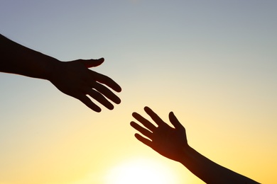 Photo of Man giving hand to woman outdoors at sunset, closeup. Help and support concept