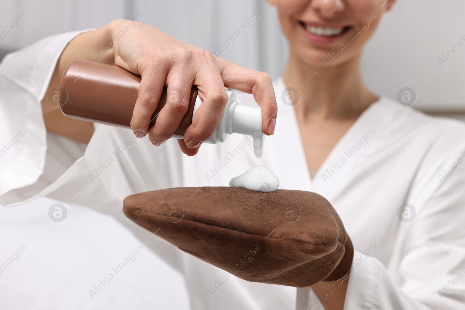 Photo of Self-tanning. Woman applying cosmetic product onto tanning mitt indoors, closeup