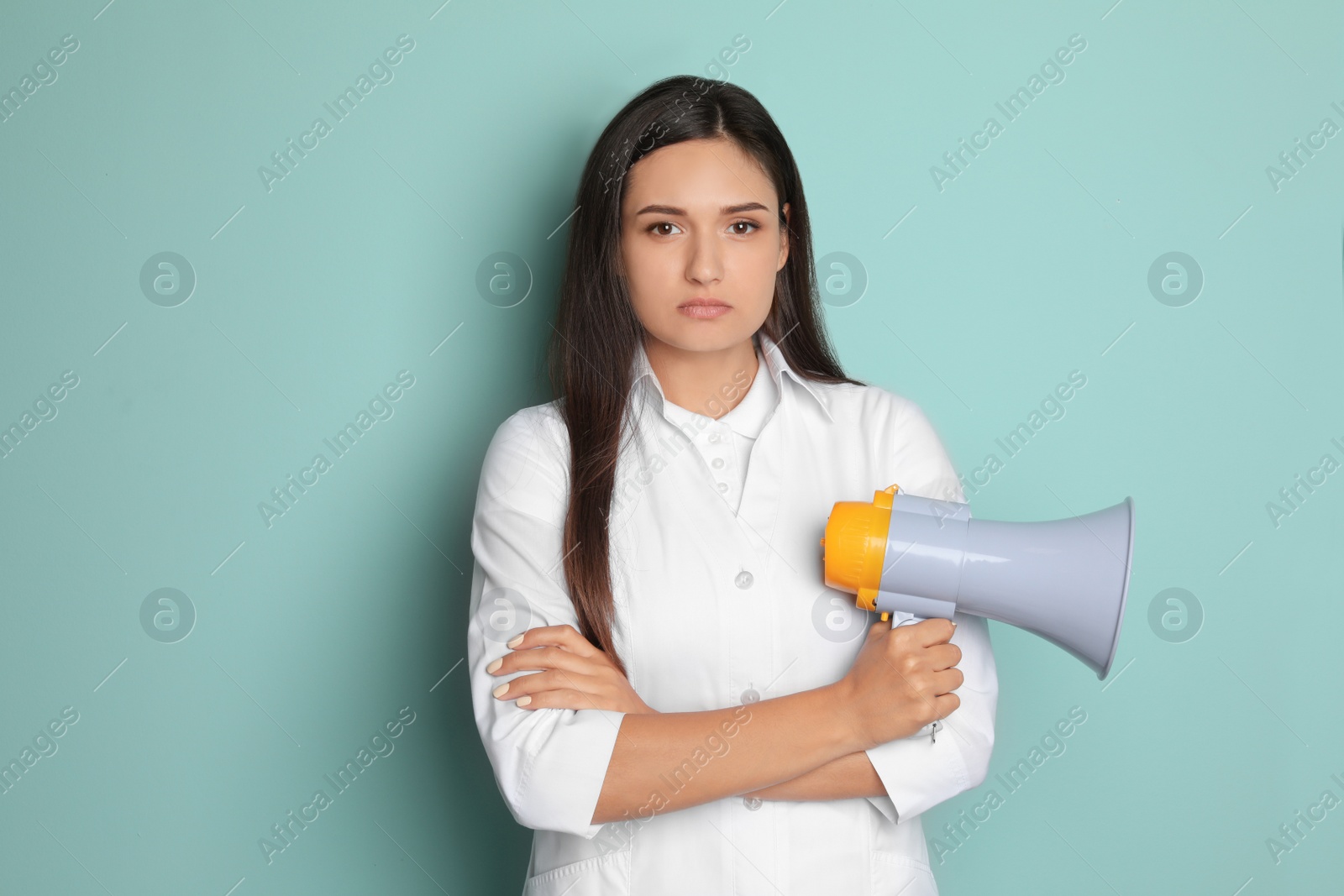 Photo of Young female doctor with megaphone on color background