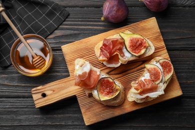 Sandwiches with ripe figs, prosciutto and cream cheese served on black wooden table, flat lay