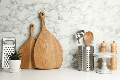 Photo of Wooden cutting boards, kitchen utensils and houseplant on white table near marble wall