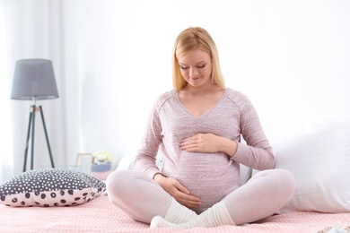 Photo of Beautiful pregnant woman sitting on bed in light room