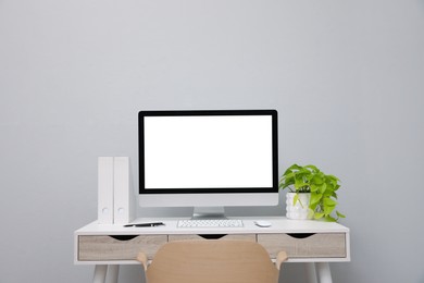 Photo of Comfortable workplace with blank computer display and plant on desk near light grey wall. Space for text