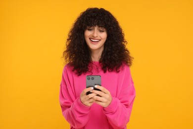 Happy young woman using smartphone on yellow background