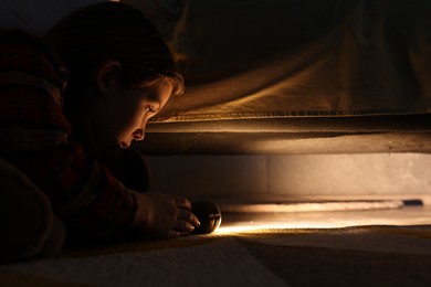 Photo of Little girl with flashlight looking for monster under bed at night