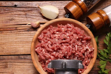 Photo of Manual meat grinder with beef mince, onion, garlic, parsley and spices on wooden table, flat lay