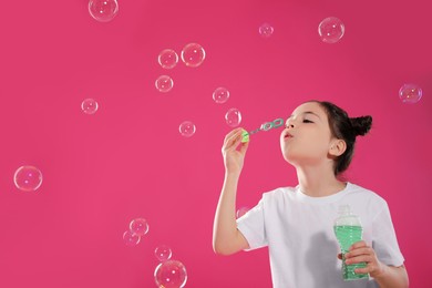 Photo of Little girl blowing soap bubbles on pink background, space for text