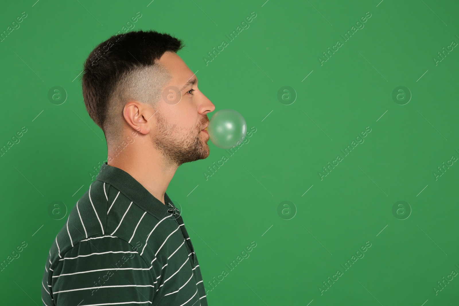 Photo of Handsome man blowing bubble gum on green background, space for text