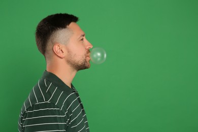 Handsome man blowing bubble gum on green background, space for text