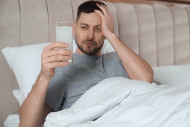 Photo of Man taking medicine for hangover in bed at home, focus on hand with glass