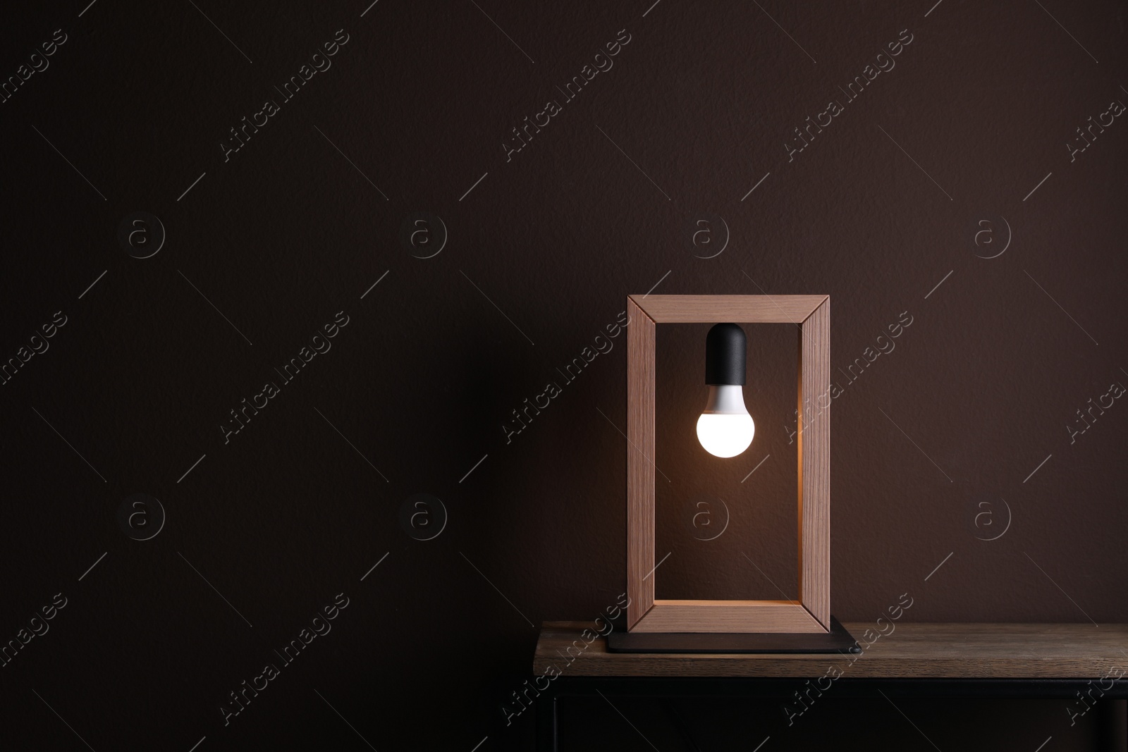 Photo of Wooden table with lamp near brown wall in room, space for text