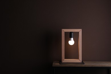 Photo of Wooden table with lamp near brown wall in room, space for text