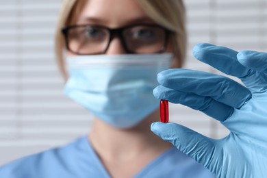 Photo of Doctor holding pill on light background, selective focus. Space for text