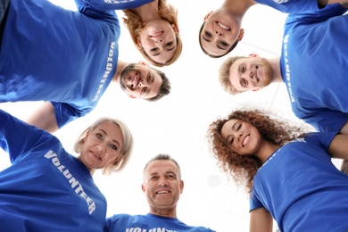 Photo of Team of volunteers joined in circle on light background, bottom view