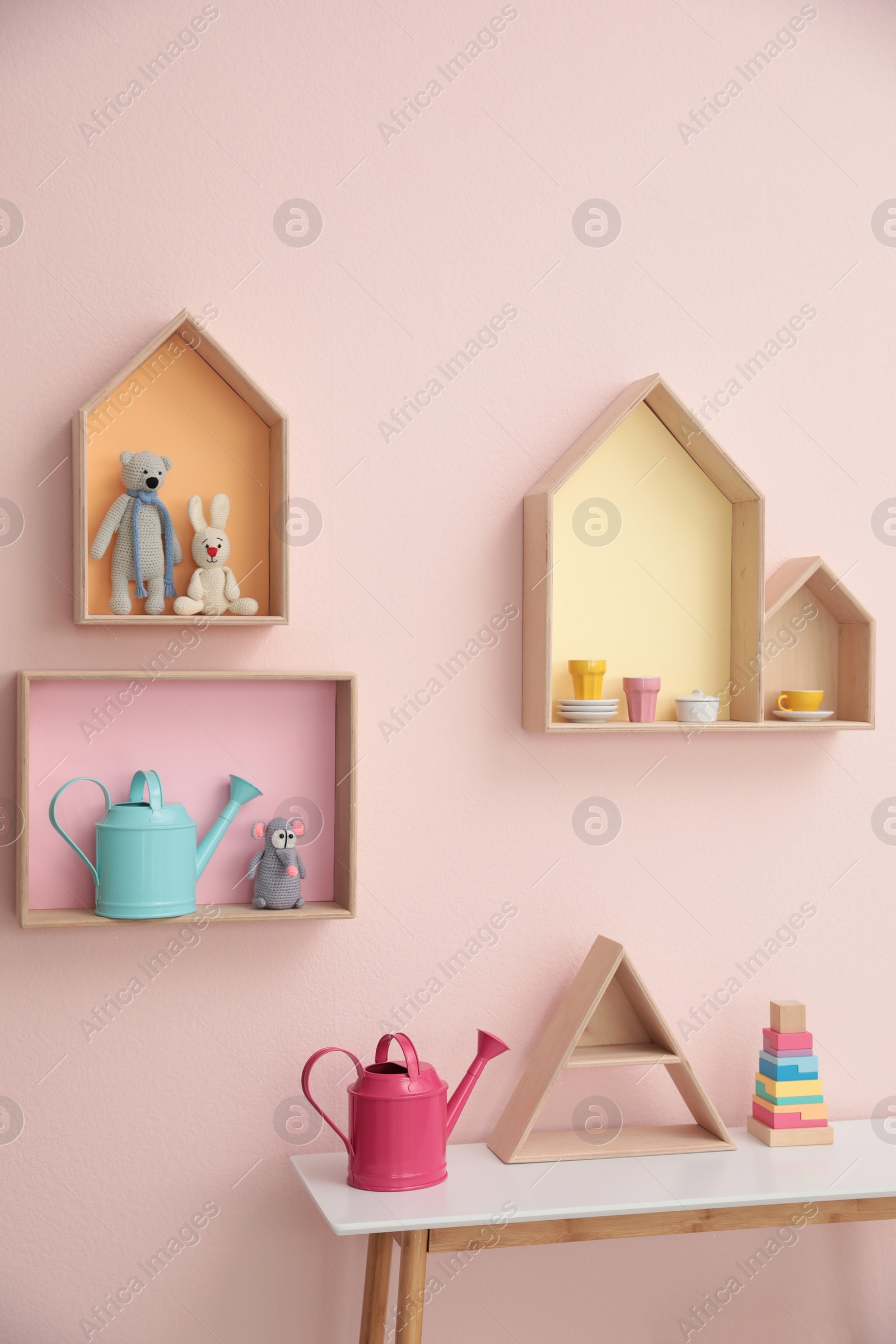 Photo of Stylish house shaped shelves with toys and wooden table indoors. Baby room interior design