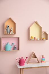Stylish house shaped shelves with toys and wooden table indoors. Baby room interior design